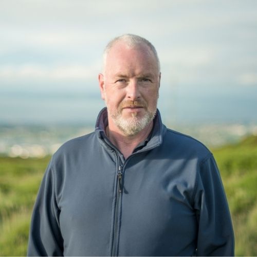 Man standing outdoors in nature with green fields.