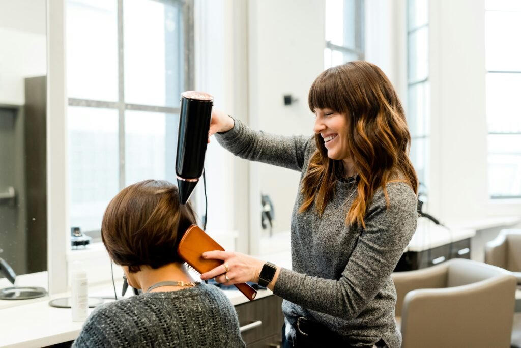 Hairdresser styling woman's hair with dryer