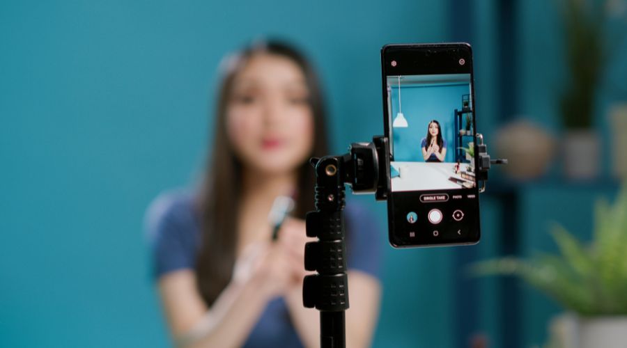 Woman filming herself with smartphone in blue room.