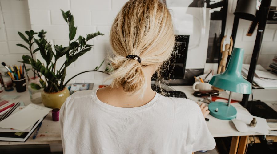 Woman working at cluttered desk, green lamp in view.