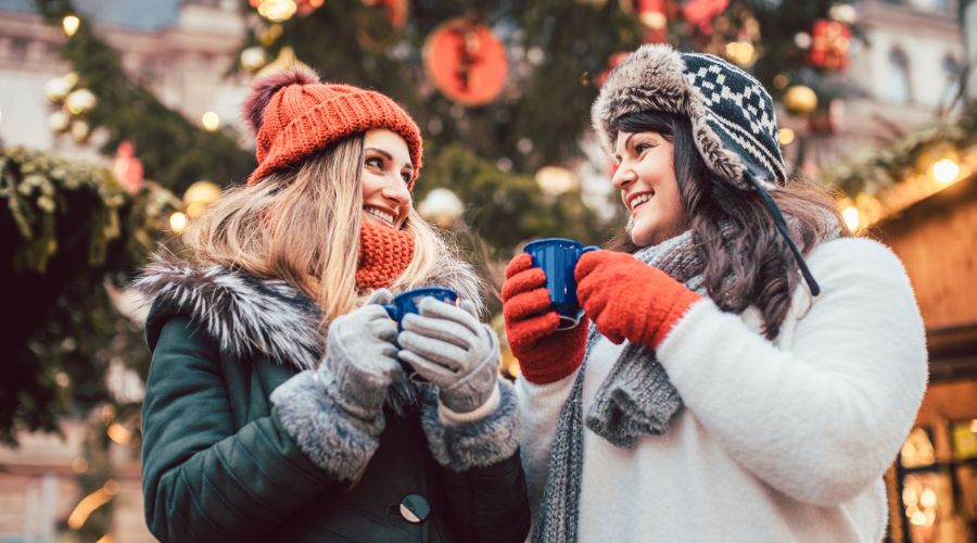 Two women enjoying hot drinks at Christmas market.