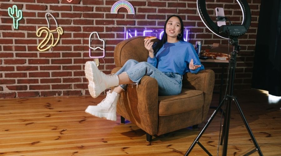 Woman eating pizza in cozy chair with neon lights.