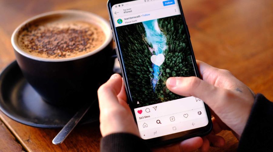 Person scrolling Instagram beside coffee cup