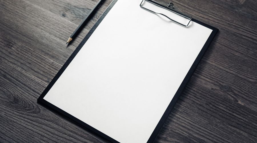 Empty clipboard and pencil on wooden desk.