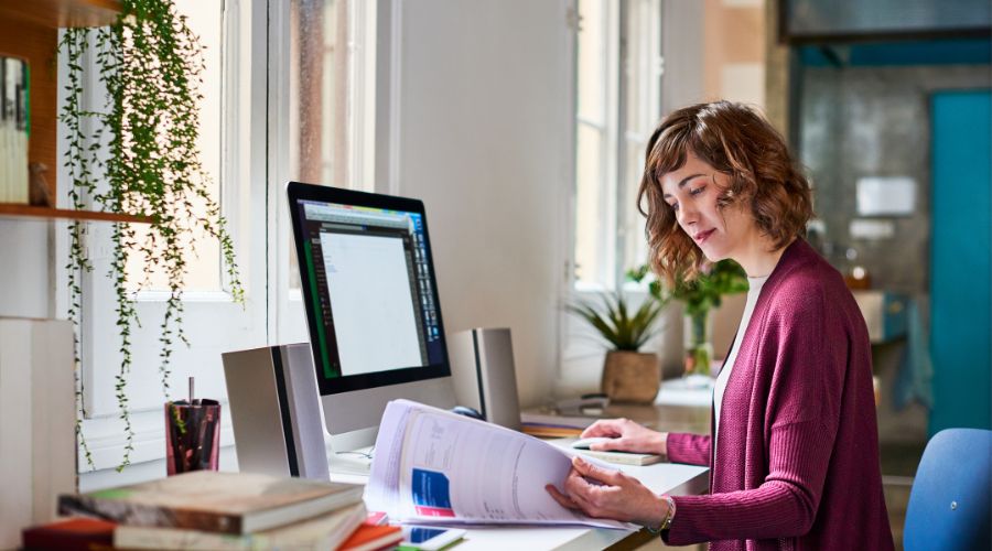 Woman working at desk with computer and book