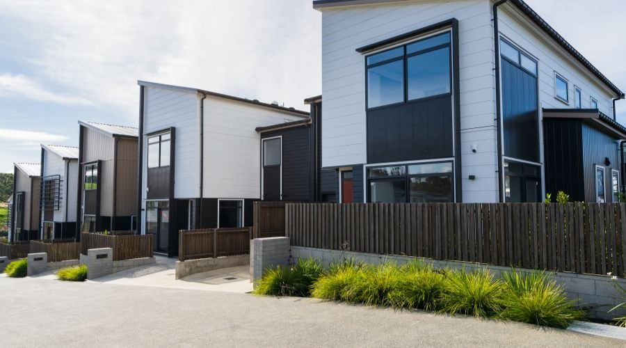 Modern townhouses with fences and greenery.