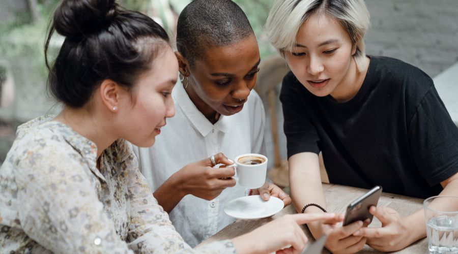 Three friends chatting over coffee, looking at phone.