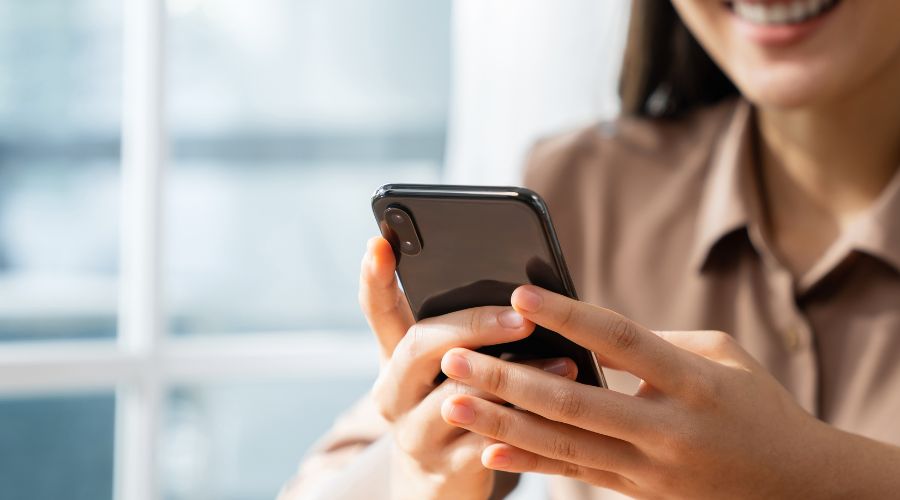 Woman smiling while using smartphone indoors.