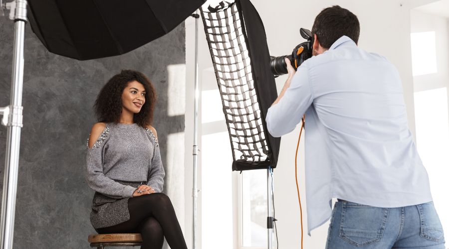 Photographer takes picture of sitting woman in studio.