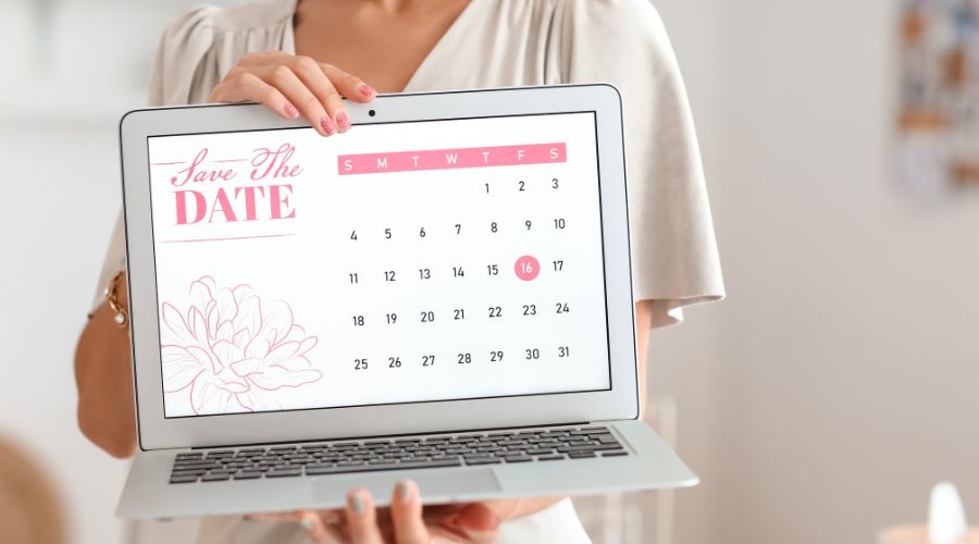 Woman holding laptop displaying save the date calendar.