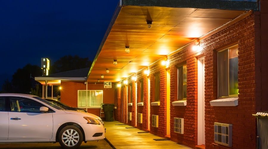 Exterior view of brick motel with parked car at night.