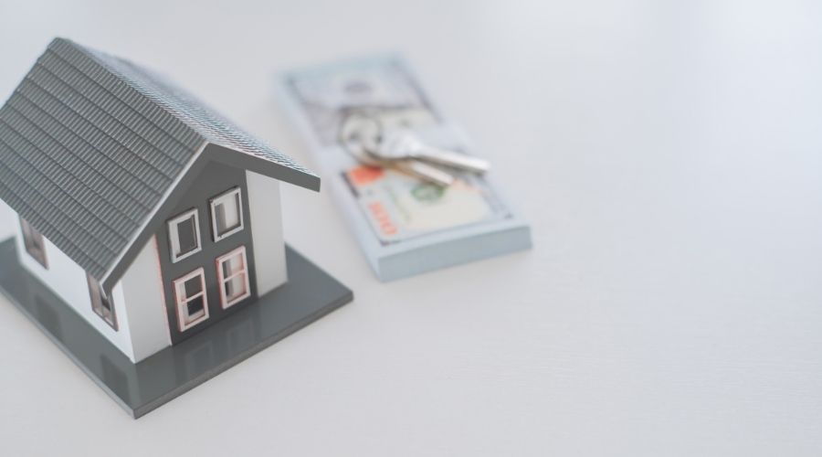 Model house, money, and keys on table.