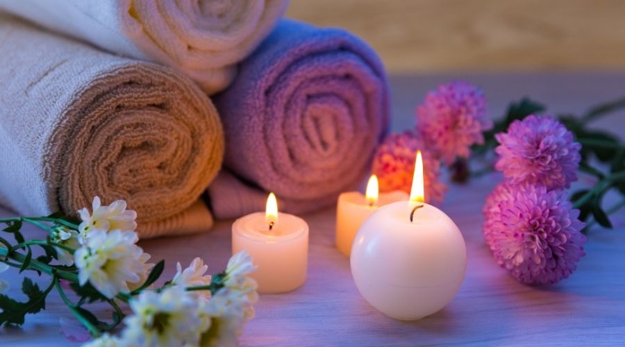 Rolled towels, lit candles, and flowers for relaxation.