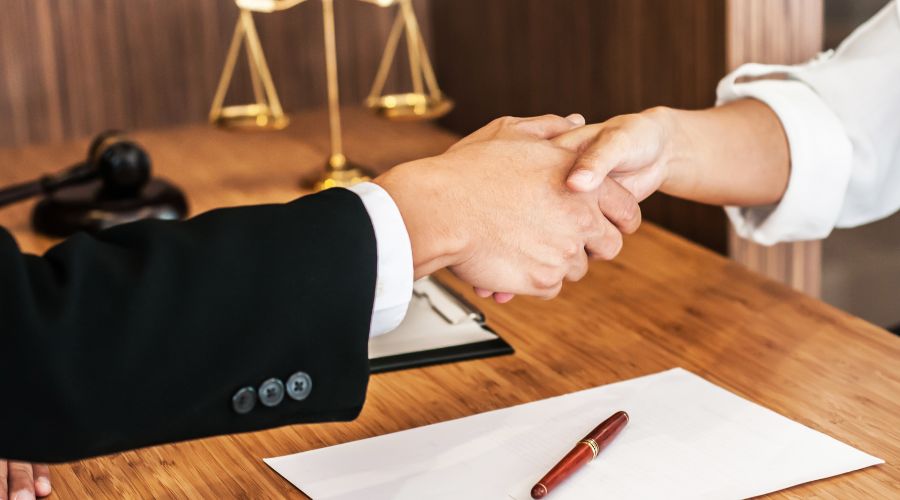 Handshake with legal documents on desk.