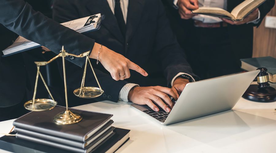 Legal professionals discussing case at laptop and books.