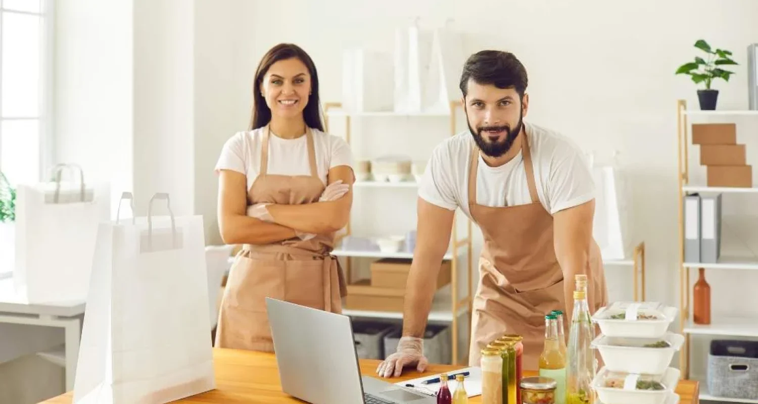 Smiling shopkeepers in aprons behind counter.