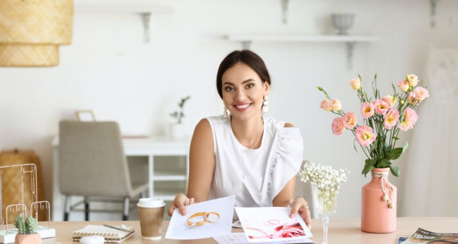 Woman smiling with jewelry designs at desk.