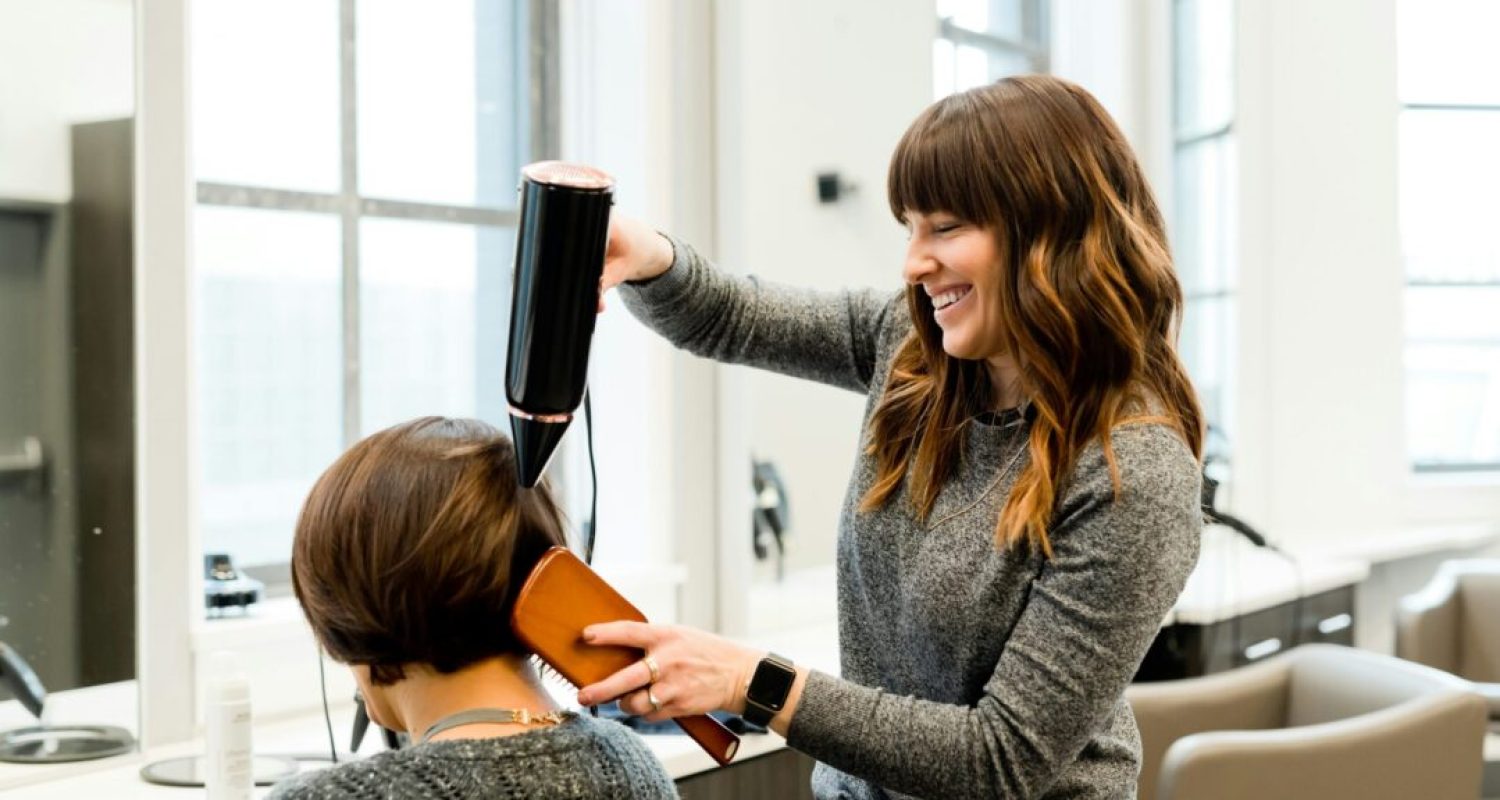 Hairdresser styling woman's hair with dryer