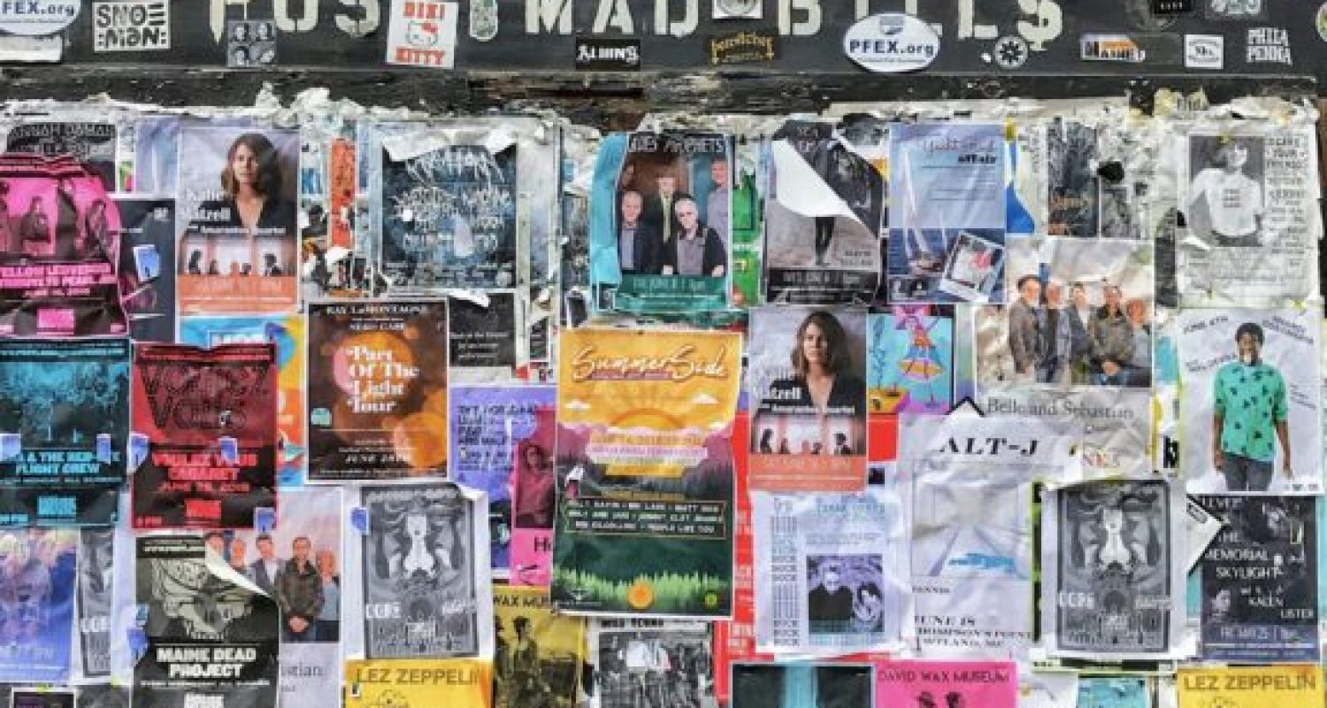 Colorful event posters on brick wall bulletin board.