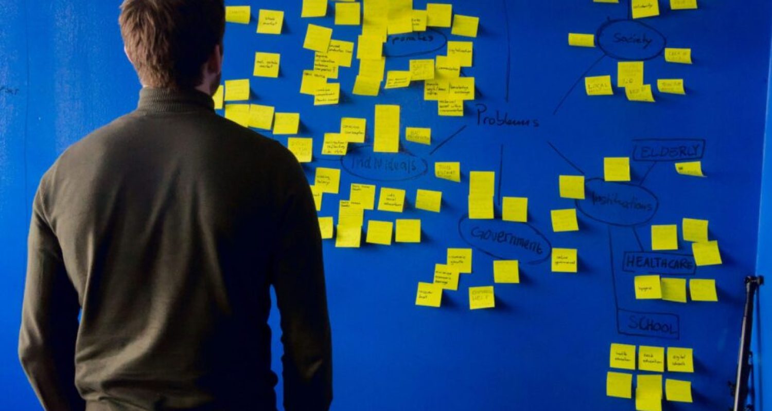 Person analyzes mind map of sticky notes on board.