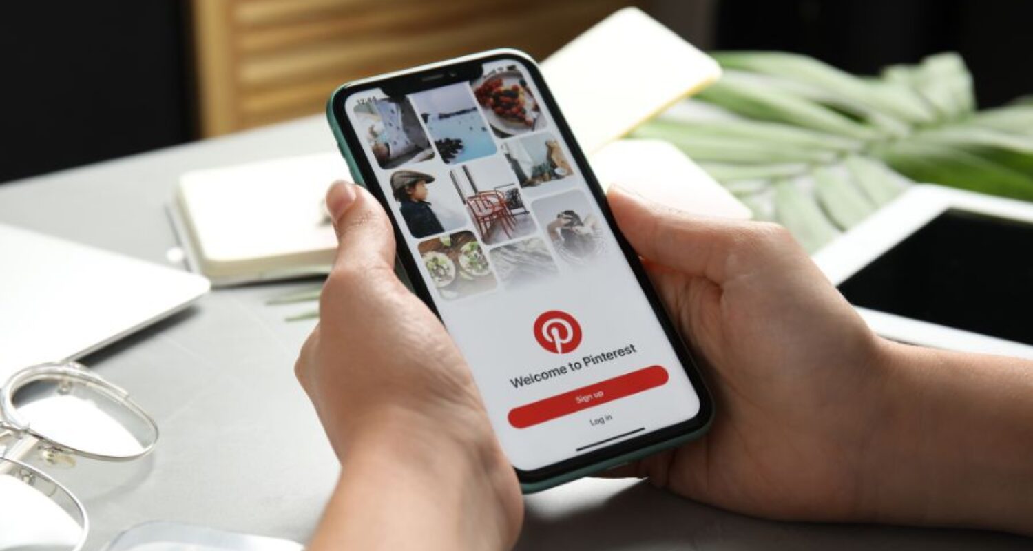 Person holding phone displaying Pinterest app login screen.