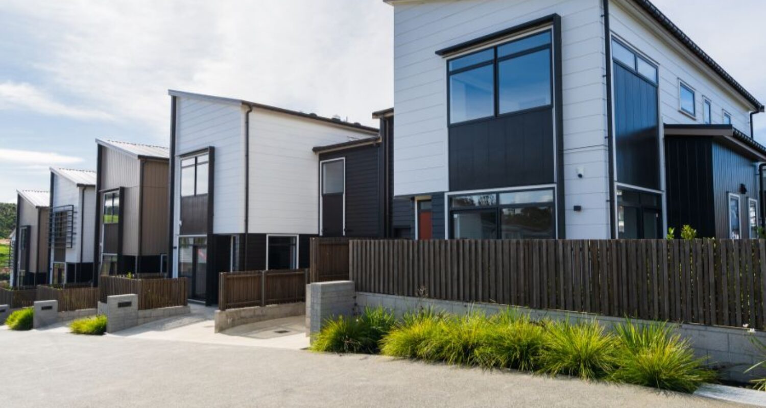 Modern townhouses with fences and greenery.