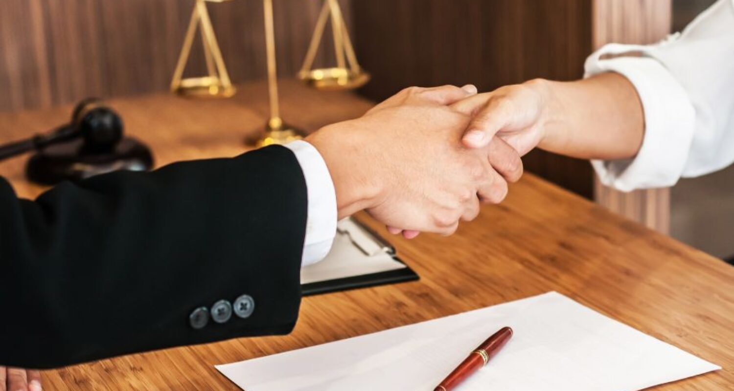 Handshake with legal documents on desk.