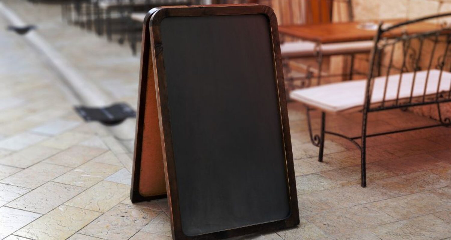 Empty chalkboard sign on outdoor cafe patio